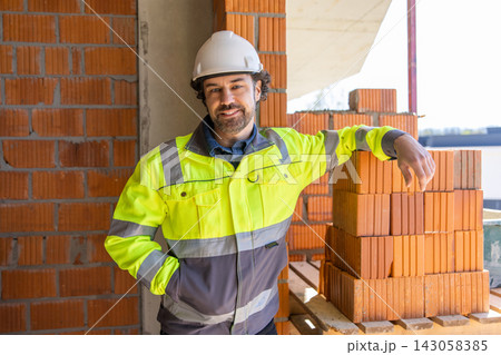 Construction worker standing beside brick stack indoors 143058385