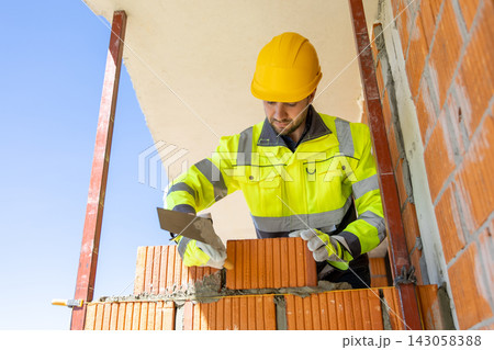 Construction worker holding trowel near brick wall 143058388