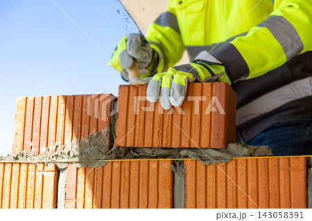 Construction worker laying red brick using trowel and mortar Construction worker laying red brick using trowel and mortar 143058391