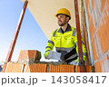 Happy builder wearing yellow hard hat holding trowel checking alignment 143058417
