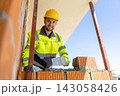 Smiling constructor wearing safety gear holding trowel looking at camera 143058426