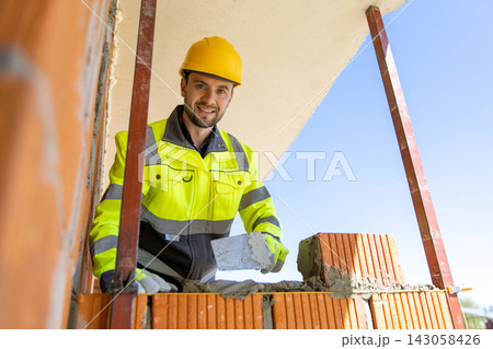 Smiling constructor wearing safety gear holding trowel looking at camera 143058426