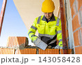 Focused bricklayer in hard hat smoothing cement mortar using steel trowel 143058428