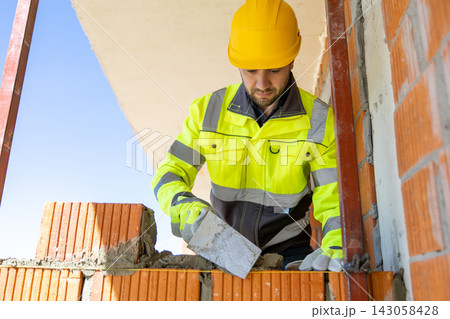 Focused bricklayer in hard hat smoothing cement mortar using steel trowel Focused bricklayer in hard hat smoothing cement mortar using steel trowel 143058428