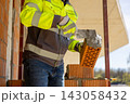 Construction worker holding trowel spreading cement mortar on ceramic block 143058432