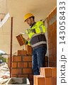 Builder in yellow safety helmet holding trowel with mortar and clay brick 143058433