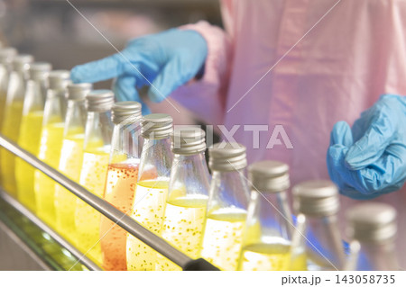 Black woman inspecting drink quality with rows of glass bottles on the automated conveyor system in manufacturing assembly line. Black woman inspecting drink quality with rows of glass bottles on the automated conveyor system in manufacturing assembly line. 143058735