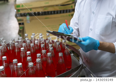 Close-up of worker hand in protective glove counting and checking drink bottle in bottle factory. Close-up of worker hand in protective glove counting and checking drink bottle in bottle factory. 143059149