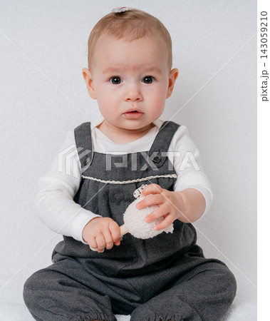 Portrait of adorable infant looking directly at camera while holding soft crochet toy. High quality child studio photography, cozy handmade materials, and innocent child smile 143059210