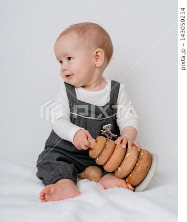 Cute infant chewing wooden stacker ring while sitting on floor during sensory play session. Montessori educational toys, natural materials, child motor skills, and happy childhood Cute infant chewing wooden stacker ring while sitting on floor during sensory play session. Montessori educational toys, natural materials, child motor skills, and happy childhood 143059214