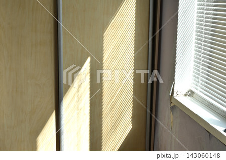 A view of an interior featuring a light-colored wooden sliding-door wardrobe and a window with blinds. 143060148