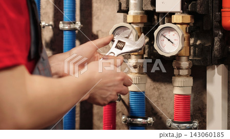 Closeup Of Plumber Or HVAC Technician Holding Adjustable Wrench Beside Heating System In Boiler Room. Residential Plumbing Installation, Repair And Maintenance Service Concept. Closeup Of Plumber Or HVAC Technician Holding Adjustable Wrench Beside Heating System In Boiler Room. Residential Plumbing Installation, Repair And Maintenance Service Concept. 143060185