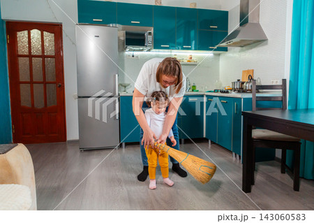 Young female educator helps a preschool girl learn to sweep with a small broom in kindergarten. The practical activity encourages coordination, independence, attention, and Montessori learning. Young female educator helps a preschool girl learn to sweep with a small broom in kindergarten. The practical activity encourages coordination, independence, attention, and Montessori learning. 143060583