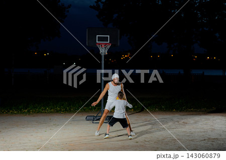 A father and son enjoy a night basketball game at a local park under bright lights focusing on teamwork and fun A father and son enjoy a night basketball game at a local park under bright lights focusing on teamwork and fun 143060879