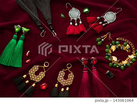 Handmade set of green,golden,black,silver and vinous bijouterie with gems, tassels, cryslals and beads, lying on the vinous velvet background, top flat view with empty place for your text Handmade set of green,golden,black,silver and vinous bijouterie with gems, tassels, cryslals and beads, lying on the vinous velvet background, top flat view with empty place for your text 143061064