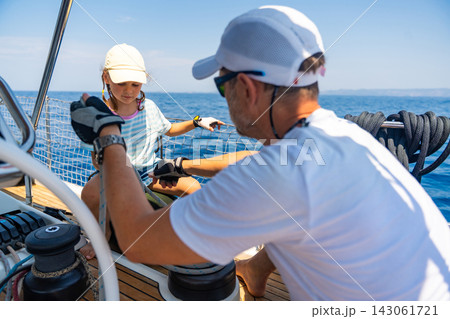 Father teaching his daughter to operate a sailing yacht during a family sea voyage. Learning practical sailing skills, teamwork and unforgettable travel experiences together. Father teaching his daughter to operate a sailing yacht during a family sea voyage. Learning practical sailing skills, teamwork and unforgettable travel experiences together. 143061721