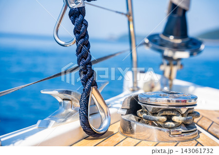 Mooring rope secured to a stainless steel cleat on the deck of a modern sailing yacht. Safe docking equipment and seamanship concept. Mooring rope secured to a stainless steel cleat on the deck of a modern sailing yacht. Safe docking equipment and seamanship concept. 143061732