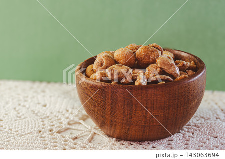 Glazed peanuts and almonds in a wooden bowl, a crunchy snack or sweet treat, a delicious mixture of nuts and caramel, isolated 143063694