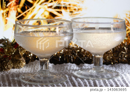Two coupe glasses filling with sparkling champagne amid golden Christmas decorations and blurred lights, creating a warm, festive, romantic holiday toast atmosphere 143063695