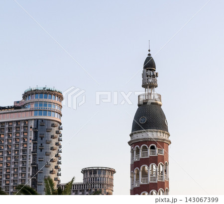 Batumi, Georgia - September 2, 2026: The architectural contrast of the historical style Chacha Tower dome standing in front of the modern Silk Road Sea Towers skyscrapers under a cloudy sky. Travel 143067399