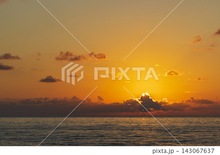 Dramatic golden sunset over the calm sea horizon with the sun bursting below dark heavy clouds. Dramatic golden sunset over the calm sea horizon with the sun bursting below dark heavy clouds. 143067637