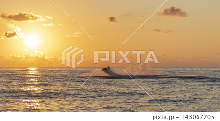 Action view of a jet ski jumping over a wave with a dramatic water splash during a beautiful golden sunset. Activity Action view of a jet ski jumping over a wave with a dramatic water splash during a beautiful golden sunset. Activity 143067705