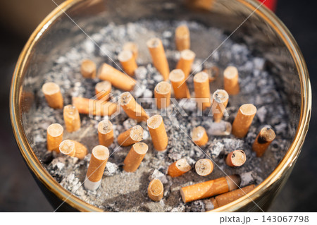 Glass ashtray filled with used cigarette butts and tobacco ashes Glass ashtray filled with used cigarette butts and tobacco ashes 143067798