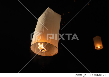 Warm glowing paper sky lantern rising at night with visible flame inside glowing thin paper and blurred lanterns in outdoor evening sky Warm glowing paper sky lantern rising at night with visible flame inside glowing thin paper and blurred lanterns in outdoor evening sky 143068177