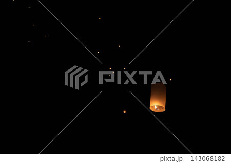 Warm glowing paper sky lantern rising at night with visible flame inside glowing thin paper and blurred lanterns in outdoor evening sky 143068182