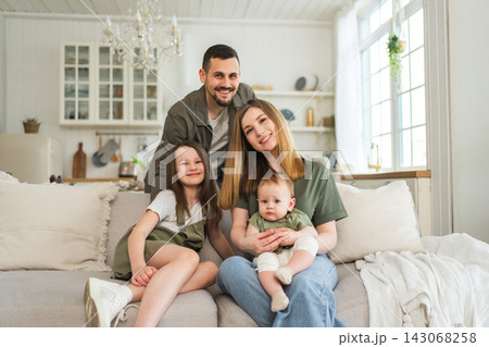 Happy family at home. Mother father two children daughters relaxing on sofa indoor. Mom dad parents baby girls kids relax playing having fun together. Family smiling laughing enjoying tender moment Happy family at home. Mother father two children daughters relaxing on sofa indoor. Mom dad parents baby girls kids relax playing having fun together. Family smiling laughing enjoying tender moment 143068258
