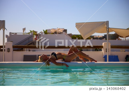 Attractive Woman in Bikini Relaxing Beside a Swimming Pool on a Sunny Resort Day 143068402