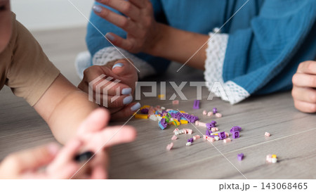 Close up view of children hands gathered around scattered colorful building blocks on wooden floor, showing playful teamwork, creative learning, soft natural indoor light, and relaxed home playtime Close up view of children hands gathered around scattered colorful building blocks on wooden floor, showing playful teamwork, creative learning, soft natural indoor light, and relaxed home playtime 143068465