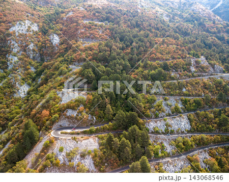 Lovcen Serpentine Montenegro traces twisting hillside route through dense autumn forest. Serpentine mountain road climbs past exposed limestone and curves, evoking peaceful travel in rugged terrain. 143068546