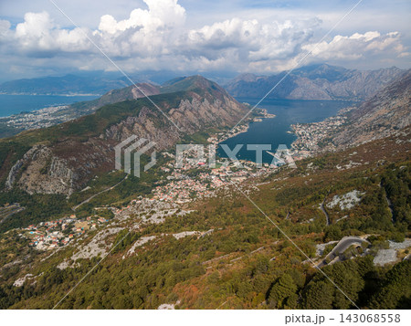 Lovcen Serpentine overlooks Kotor, with bay, city, and mountains spread below. Mountain road winds through rocky slopes, creating dramatic Montenegro panorama for travel and landscape buyers. 143068558