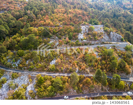Lovcen Serpentine Montenegro winds across rocky forest slopes. Mountain road bends through autumn colored hillside, with cars on paved curves and stone retaining walls framing dramatic alpine terrain. Lovcen Serpentine Montenegro winds across rocky forest slopes. Mountain road bends through autumn colored hillside, with cars on paved curves and stone retaining walls framing dramatic alpine terrain. 143068561