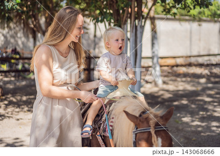 Excited little boy enjoys pony riding with his mother's support. Happy riding experiences and outdoor family fun. Excited little boy enjoys pony riding with his mother's support. Happy riding experiences and outdoor family fun. 143068666