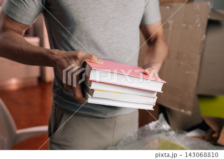 Close-up cropped shot of person holding paperback books, preparing them for packing into cardboard boxes during home relocation, focusing on organization and decluttering. Close-up cropped shot of person holding paperback books, preparing them for packing into cardboard boxes during home relocation, focusing on organization and decluttering. 143068810