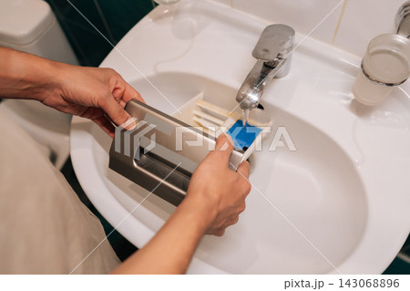 Male hands cleaning washing machine detergent dispenser tray in bathroom sink, performing household chore and maintaining domestic life routine. Concept of household chores. Male hands cleaning washing machine detergent dispenser tray in bathroom sink, performing household chore and maintaining domestic life routine. Concept of household chores. 143068896