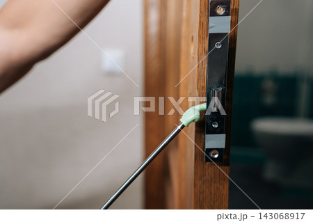 Close-up of unrecognizable person learning and performing door lock and handle replacement, using telescopic pointer for detailed instruction during home improvement training session. 143068917