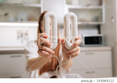 Woman holding electric shoe dryer, demonstrating modern gadget for footwear care, quickly drying shoes and boots to maintain hygiene and comfort in household setting. 143069112