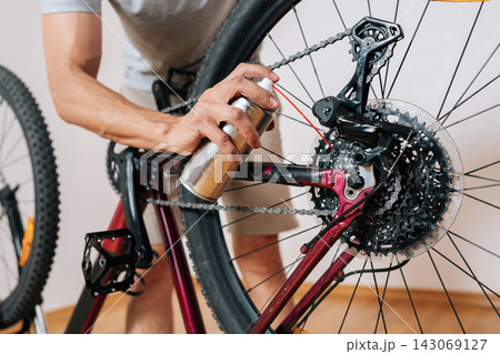 Bicycle repair and service concept. Focused cyclist taking care of bike, cleaning and oiling drivetrain components in home garage for smooth performance. Do it yourself hobby, closeup, cropped shot. 143069127