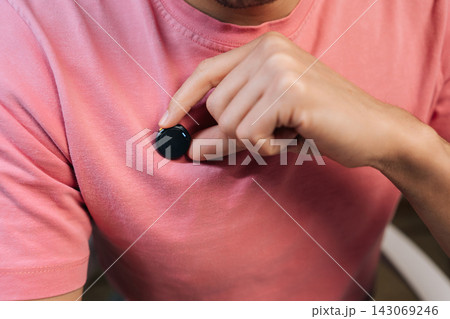 Person attaching modern wireless lavalier microphone with magnet to pink t-shirt for interview or broadcast, preparing audio equipment for recording. Person attaching modern wireless lavalier microphone with magnet to pink t-shirt for interview or broadcast, preparing audio equipment for recording. 143069246