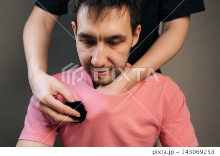 Man preparing for recording session by placing small, modern wireless lavalier microphone onto pink shirt using a magnetic clip for optimal sound quality. Man preparing for recording session by placing small, modern wireless lavalier microphone onto pink shirt using a magnetic clip for optimal sound quality. 143069258