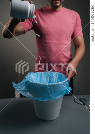Vertical cropped shot of man disposing of medication bottles and expired pharmaceutical drugs into blue trash bag, managing waste and showing responsible healthcare practice, close-up. Vertical cropped shot of man disposing of medication bottles and expired pharmaceutical drugs into blue trash bag, managing waste and showing responsible healthcare practice, close-up. 143069260