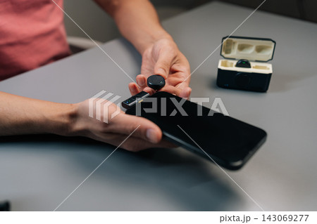 Close-up cropped shot of person setting up professional audio recording system by plugging wireless lavalier microphone receiver with adapter into mobile phone for interviews. 143069277