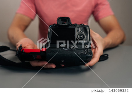 Cropped of photographer holding camera with battery grip, inserting red external battery holder, showcasing essential gear for photographers needing extended power and improved ergonomics. Cropped of photographer holding camera with battery grip, inserting red external battery holder, showcasing essential gear for photographers needing extended power and improved ergonomics. 143069322