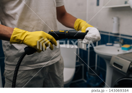 Man wearing yellow rubber gloves holding steam cleaner, preparing to sanitize and deep clean bathroom, focusing on hygiene, domestic chores and household maintenance. 143069384