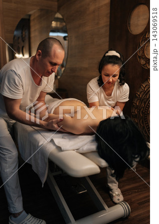 Vertical portrait of male and female professional masseurs giving four hand synchronized massage to woman patient in dark spa salon for deep relaxation, muscle relief, overall wellness. Vertical portrait of male and female professional masseurs giving four hand synchronized massage to woman patient in dark spa salon for deep relaxation, muscle relief, overall wellness. 143069518