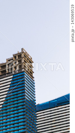 Low angle view of modern blue glass skyscrapers under construction showing top concrete frames against a clear sky. Industrial Low angle view of modern blue glass skyscrapers under construction showing top concrete frames against a clear sky. Industrial 143069519
