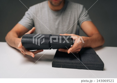 Close-up cropped shot of man holding black acoustic foam panel, examining sound absorbing material for noise control, soundproofing, insulation in dark recording studio or home environment. 143069521